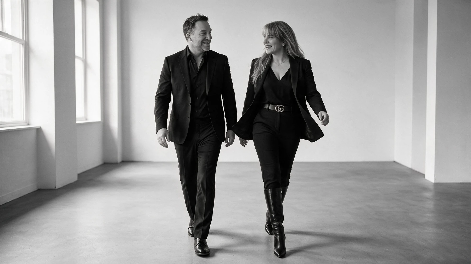 Summer and Randy Branam walking together in tailored black outfits, smiling at one another in a monochrome studio portrait